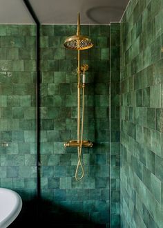 a green tiled bathroom with a gold shower head and faucet in the corner