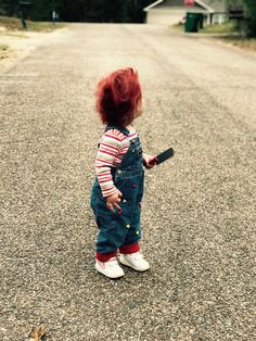 a small child with red hair standing in the middle of a road holding a bat