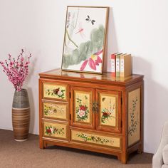 a wooden cabinet with flowers painted on the doors and drawers next to a vase with pink flowers