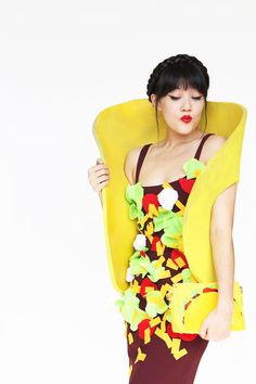 a woman in a dress with flowers on it and a banana shaped body pillow over her head