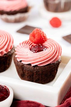 two cupcakes with pink frosting and a strawberry on top are sitting on a white plate