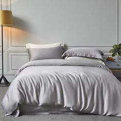 a white bed with grey sheets and pillows