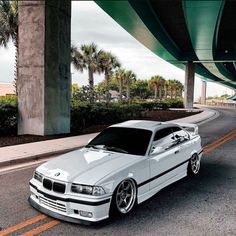 a white car parked under a bridge next to palm trees