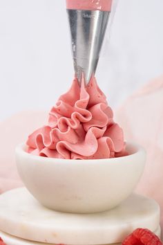 a white bowl filled with pink icing next to raspberries