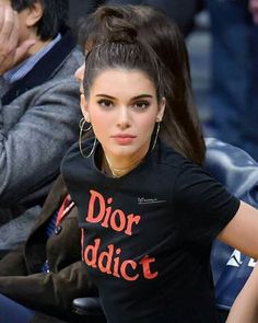 a woman sitting down with her hand on her hip while wearing large hoop earrings and a dior t - shirt