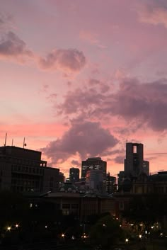 the city skyline is lit up at night with pink and purple clouds in the sky