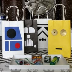 some paper bags are sitting on a table with star wars items in them and one bag is yellow, the other blue