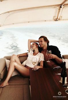 a man and woman sitting on top of a boat holding glasses of wine in their hands