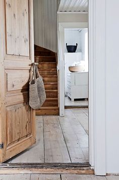 an open door leading to a white room with wooden floors and stairs in the background