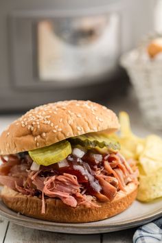 a pulled pork sandwich with pickles and ketchup on a plate next to potato chips