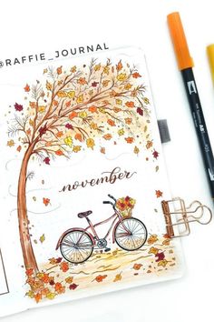 a notepad with an autumn tree and bicycle on it next to two markers that read,