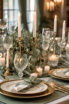 Elegant dining table set with candles, greenery, crystal glasses, and gold-rimmed plates.