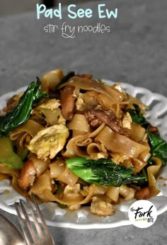 a white plate topped with pasta and veggies next to a fork on a table