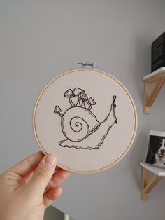 a person holding up a embroidery project with a snail on it