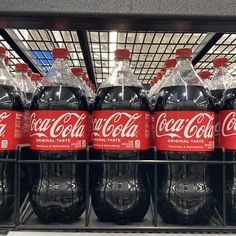 several bottles of coca - cola are on display in a grocery store, one is red and the other is black