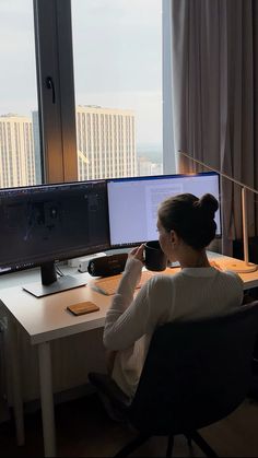 a woman sitting at a desk in front of a computer monitor with a view of the city