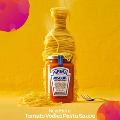 a jar filled with spaghetti and sauce sitting on top of a yellow table next to a fork