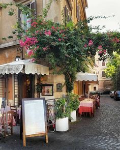 an outdoor cafe with tables and umbrellas on the side of the street in front of a building