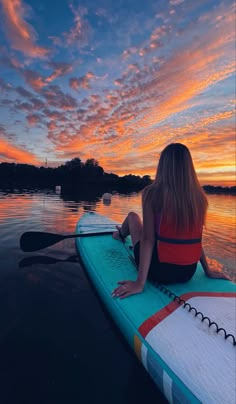 a woman sitting on top of a surfboard in the water at sunset with her back to the camera