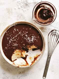 a bowl filled with chocolate pudding next to a whisk and two spoons