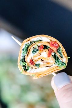 a hand holding a tortilla filled with spinach and cheese on a toothpick