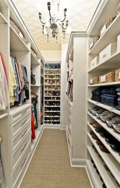 a walk - in closet with white shelves and drawers, chandelier hanging from the ceiling