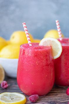 two glasses filled with raspberry lemonade next to sliced lemons and strawberries