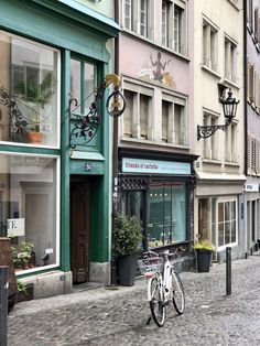 a bicycle parked in front of a store on a cobblestone street next to tall buildings