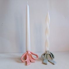 two white candles with pink and grey handles next to each other on a white surface