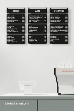 three black and white menus on the wall above a coffee shop counter with drinks in front of it