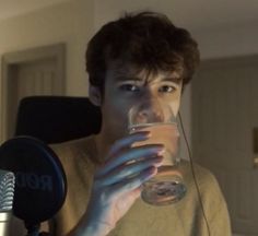 a young man drinking from a glass in front of a microphone