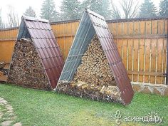 two large piles of firewood sit in the back yard next to a wooden fence