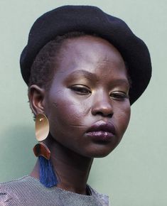 a woman with black hair and a hat on top of her head wearing gold earrings