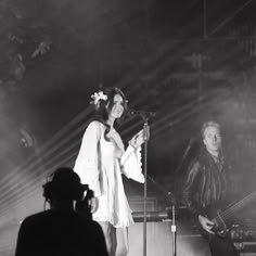 a woman standing next to a man holding a guitar on top of a stage in front of a microphone