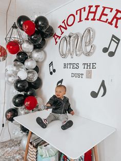 a little boy sitting on top of a table next to a wall with balloons and musical notes