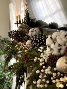 a christmas garland with pine cones, balls and lights on it in front of a window