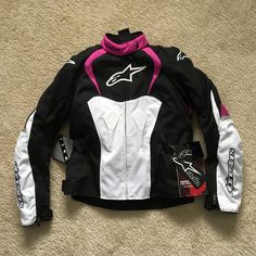 a black, white and pink alpine jacket laying on the floor next to a pair of gloves