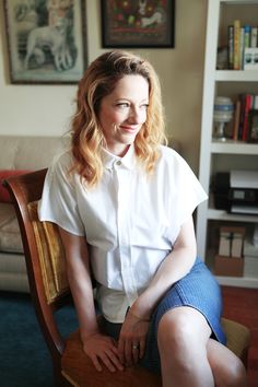 a woman sitting on top of a wooden chair in front of a bookshelf