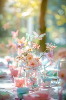 the table is set with pink and blue flowers in vases, tea cups, and saucers