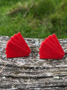 two red earrings sitting on top of a piece of wood