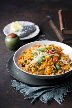 a white bowl filled with pasta and veggies on top of a black plate