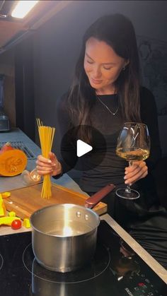 a woman standing in front of a stove holding a glass of wine and some pasta