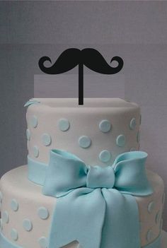 a three tiered cake decorated with blue and white polka dots, bows and a little man topper