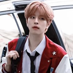 a young man wearing a red vest and black tie standing in front of a car