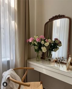 a white desk topped with a mirror next to a vase filled with pink and white flowers