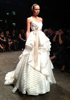 a woman is walking down the runway wearing a white dress with a big bow on it