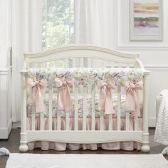 a white crib with pink bows on it in a room next to a window