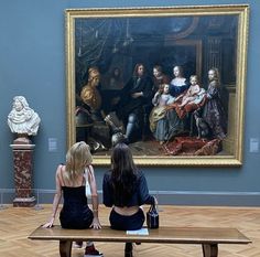 two women sitting on a bench in front of a painting