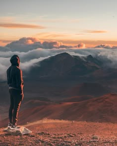 a man standing on top of a mountain looking out at the clouds in the distance