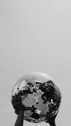 a person holding up a disco ball in front of a gray sky with no clouds